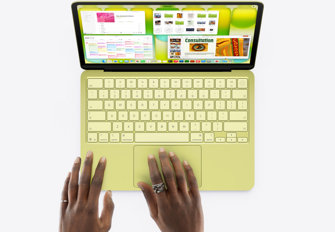 MacBook Neo citrusa krāsā, kādas personas roka uz skārienpaliktņa, ir atvērti vairāki logi, to skaitā Music, Calendar un Microsoft PowerPoint aplikācijas