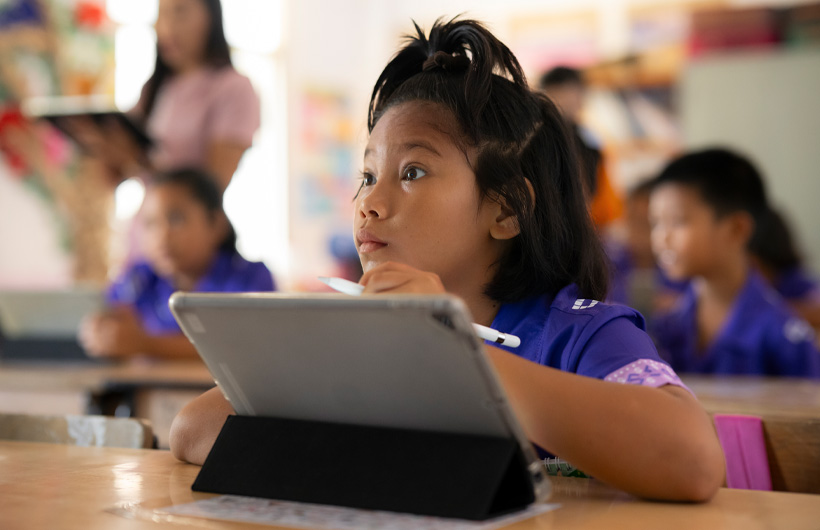Una niña mira hacia delante y presta atención durante una clase desde su pupitre. Está usando un iPad y un Apple Pencil.