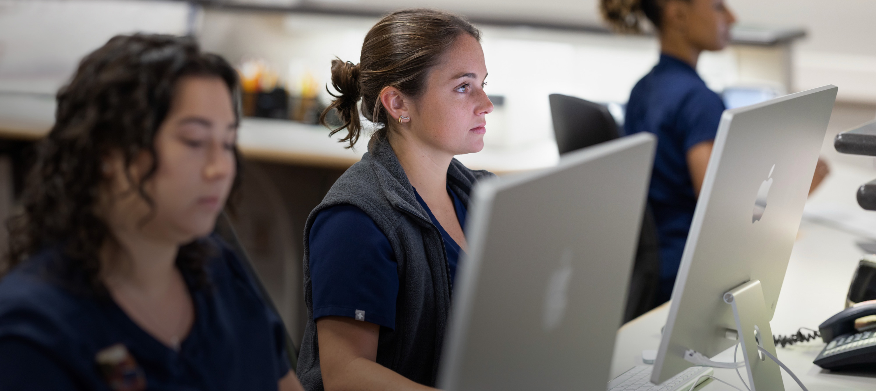 Trois infirmières travaillant derrière des écrans d’iMac.
