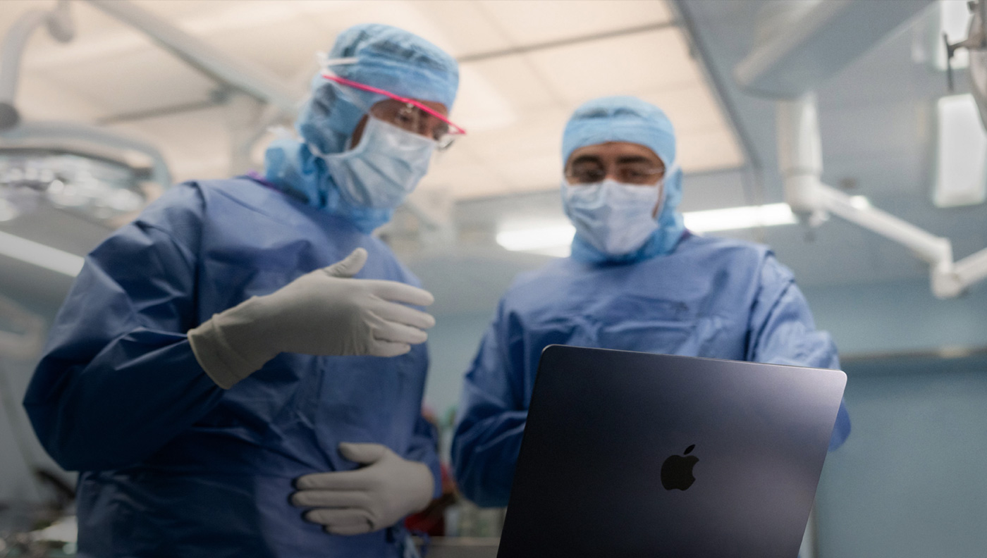 Zwei Chirurgen im OP sprechen über die Inhalte auf dem Display eines MacBook Pro.