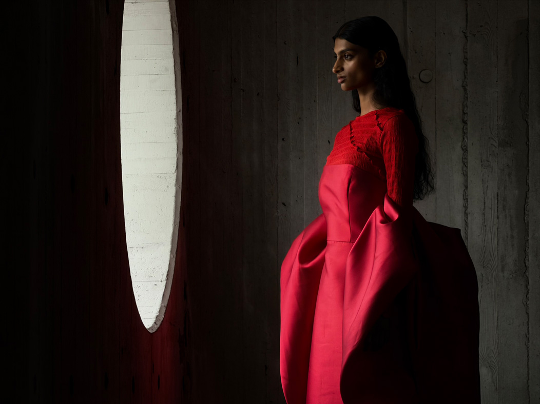 Femme portant une longue robe rouge photographiée dans une pièce vide. L’app Photos montre les distances focales pour illustrer les capacités du système caméra Pro : 200 mm