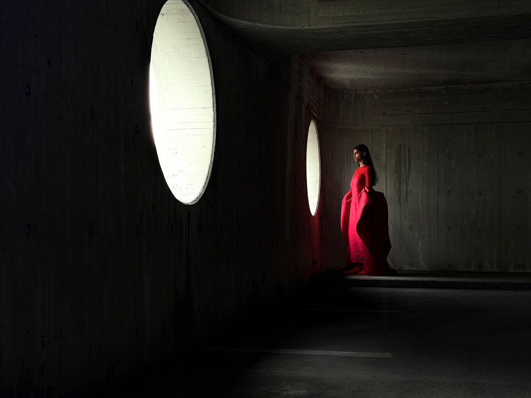 Femme portant une longue robe rouge photographiée dans une pièce vide. L’app Photos montre les distances focales pour illustrer les capacités du système caméra Pro : 48 mm