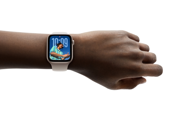 Zbliżenie na nadgarstek z zegarkiem Apple Watch w kolorze srebrnym z gumowym paskiem. Na zegarku można podziwiać nowy dizajn aplikacji Czas z wykorzystaniem technologii Liquid Glass.